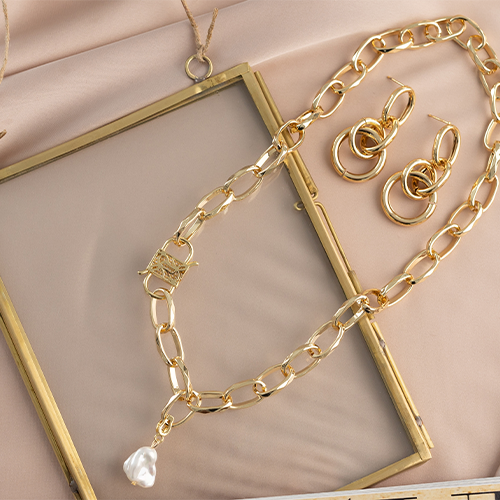 Chunky gold chain necklace featuring a white baroque pearl pendant with matching gold link earrings.