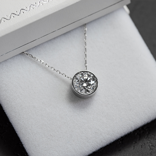 Classic bezel-set round diamond solitaire pendant on a white gold chain resting in a luxury jewelry gift box.