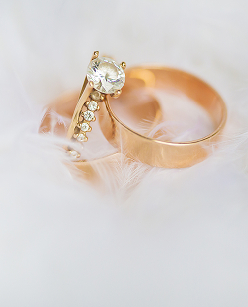 Classic yellow gold round brilliant diamond engagement ring and matching plain wedding bands resting on soft white feathers.